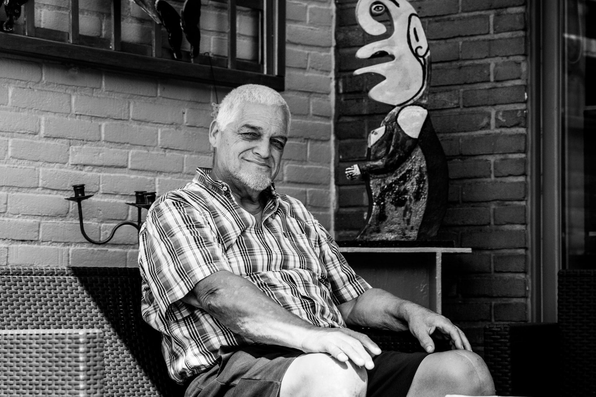 Zwart-witportret van een lachende man op een terras naast een kunstwerk